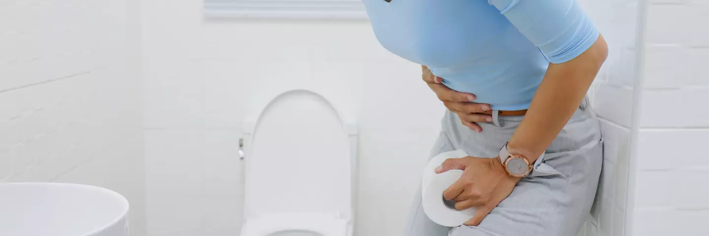 Žena s bolestí břicha drží toaletní papír u záchoda