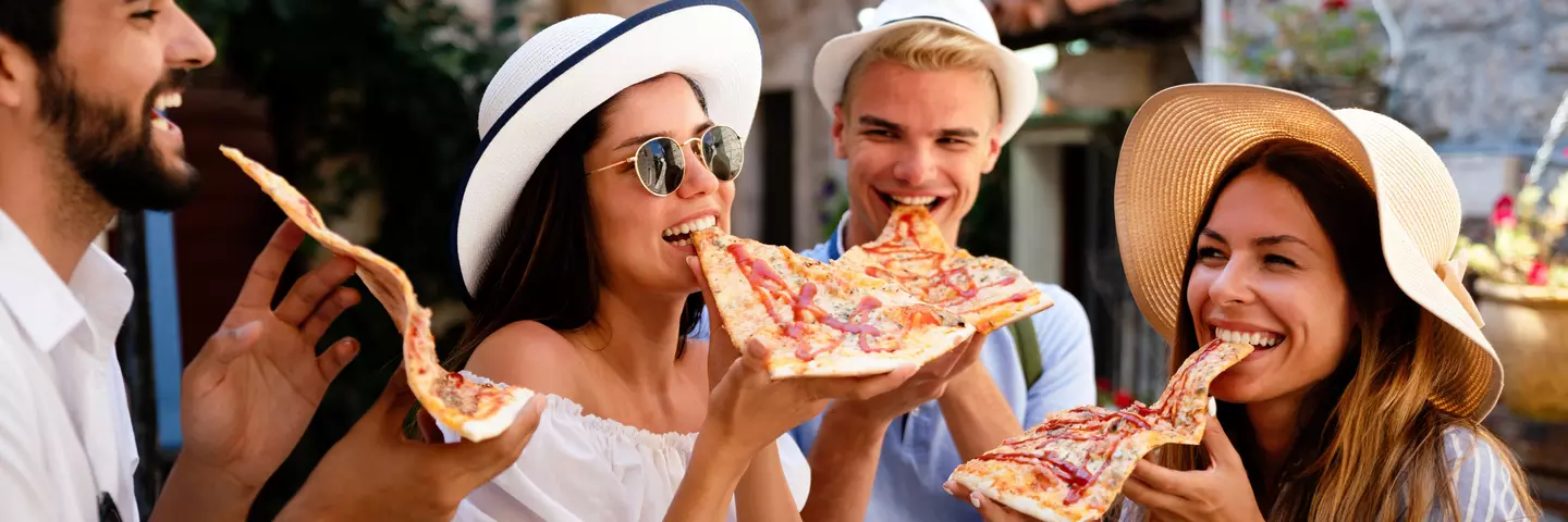 Skupina mladých lidí na dovolené se směje a jí pizzu