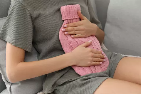 Žena si nahřívá břicho nahřívacím polštářkem