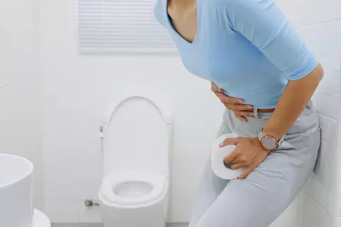 Žena s bolestí břicha drží toaletní papír u záchoda