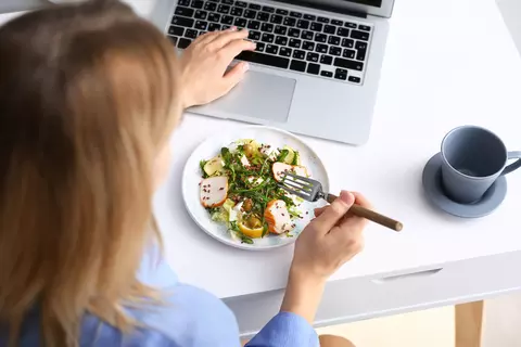 Mladá žena pracuje na počítači a obědvá u toho