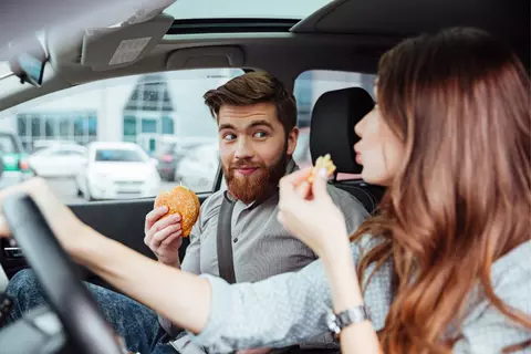 Dvojice žena muž sedí v autě a jedí fastfood