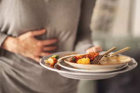 Žena se drží za břicho a v druhé ruce drží talíře od jídla Gaspan